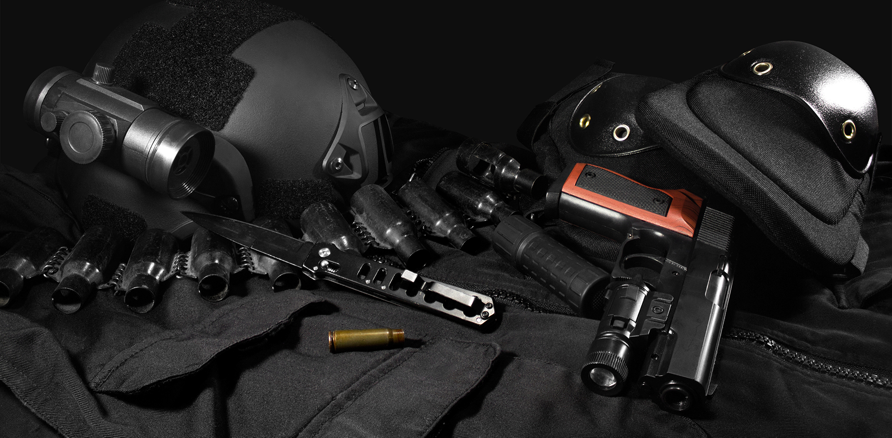 Tactical gear laying composition. Black military ammunition tactical gun, helmet, gloves, cartridge belt, bandolier, gun shell, knife, binocular and knee protection laying on a black table.